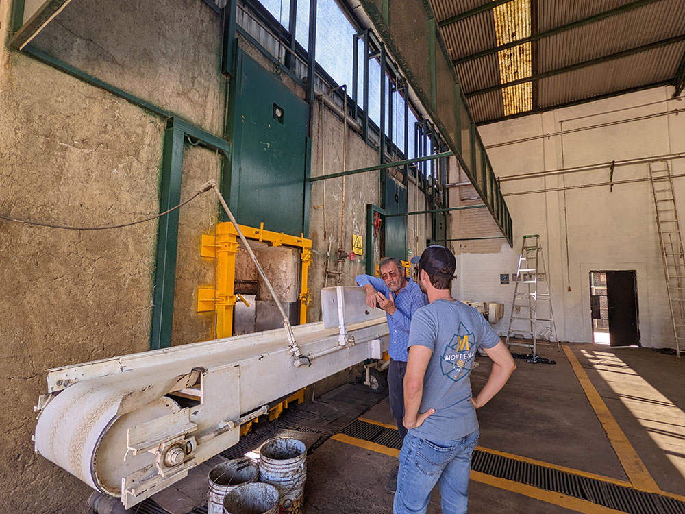 Inside the distillery, two men standing next to a conveyor belt where the piñas are cut